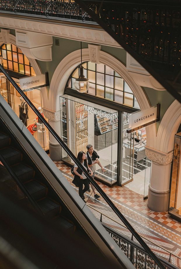Shoppers on escalator in ornate luxury shopping arcade with designer stores